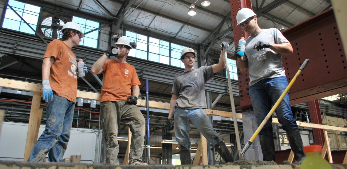 four men in construction hats and gloves standing at site with shovels