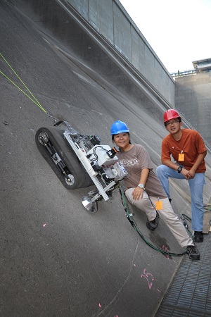 two people in hardhats standing on incline with robotic crawler