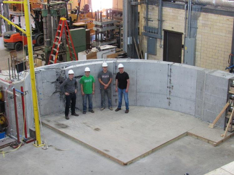 4 men in hardhats in front of curved concrete structure
